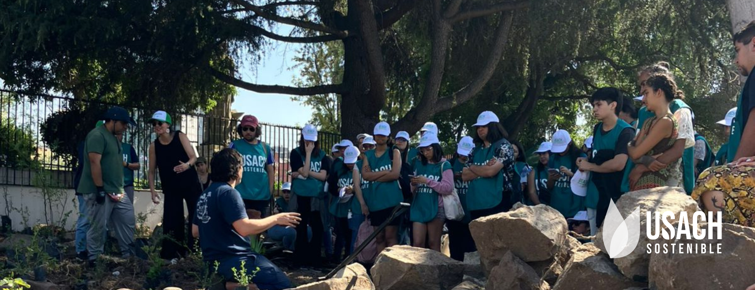 Estudiantes con pecheras verdes de Usach Sostenible escuchando activamente charla previo a actividades de plantación. 